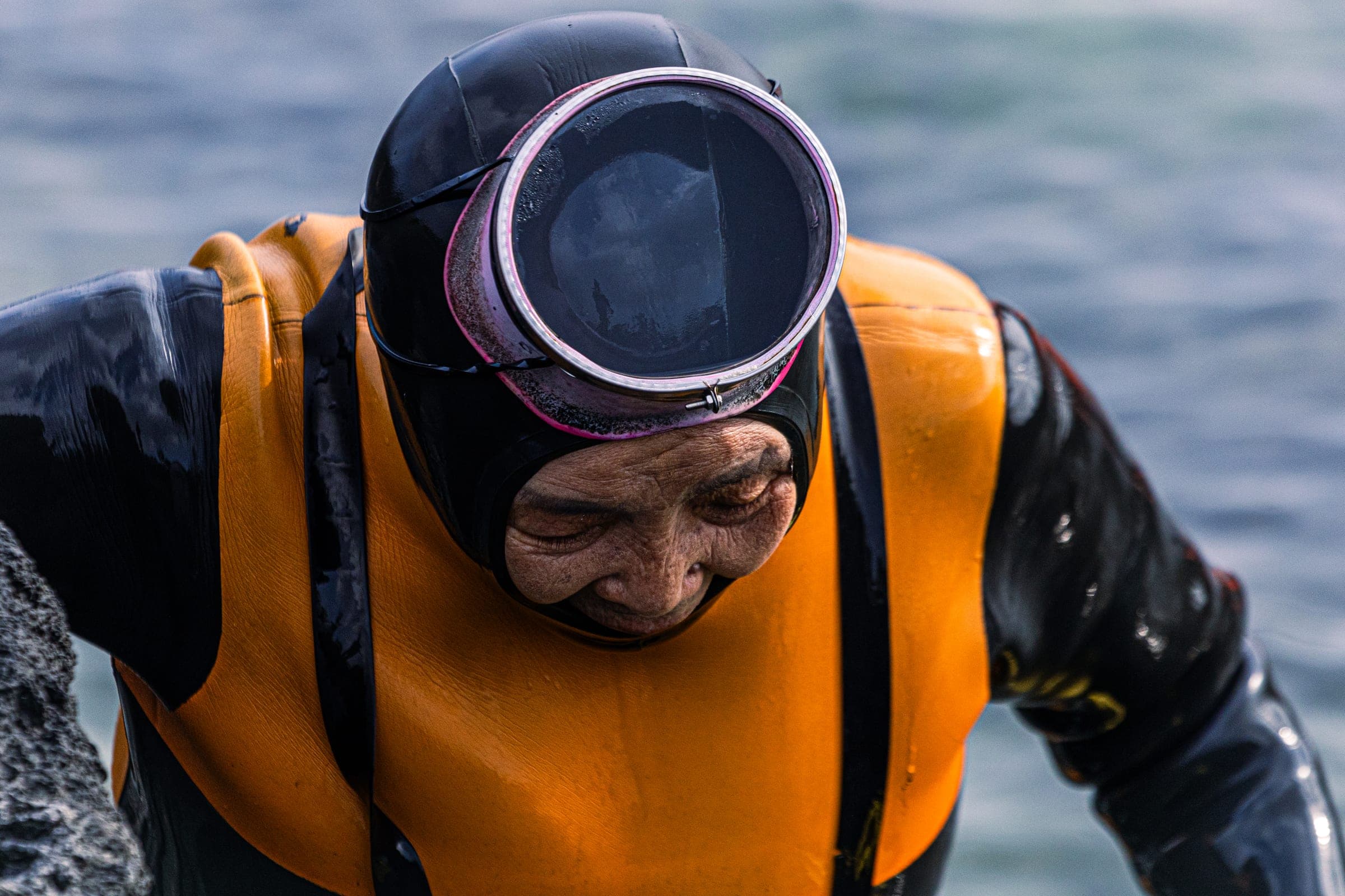An 83-year-old haenyeo, one of the women divers of Jeju, coming out of the sea in a black wetsuit, orange vest and round mask