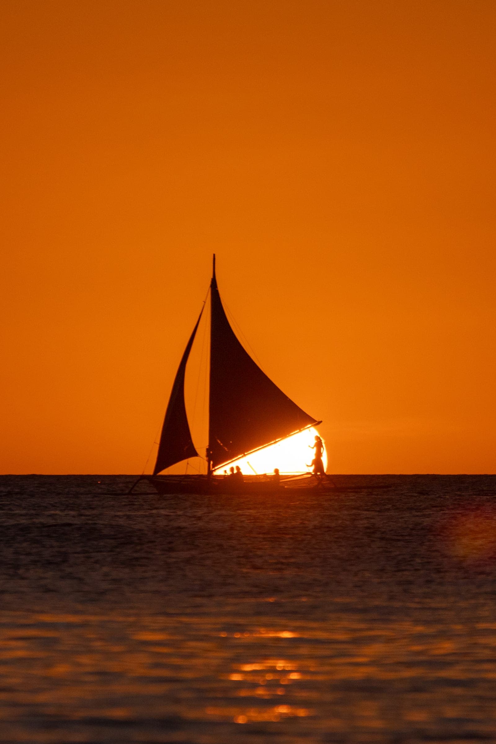 A sailing boat in silhouette on an orange sea at sunset