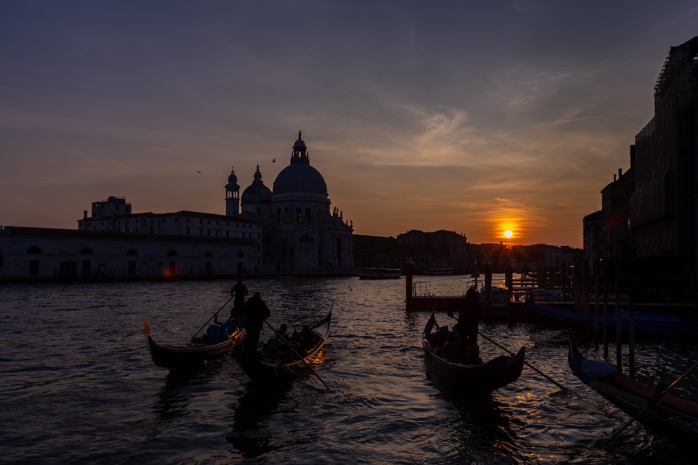 Gondolas on a canal at sunset, a domed church on the far bank