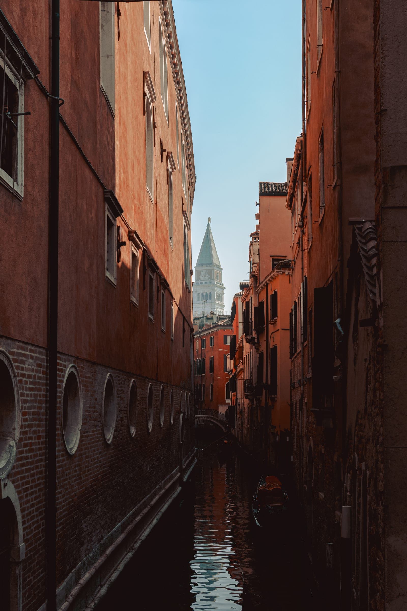 A narrow canal between red brick walls, a bell tower at the end