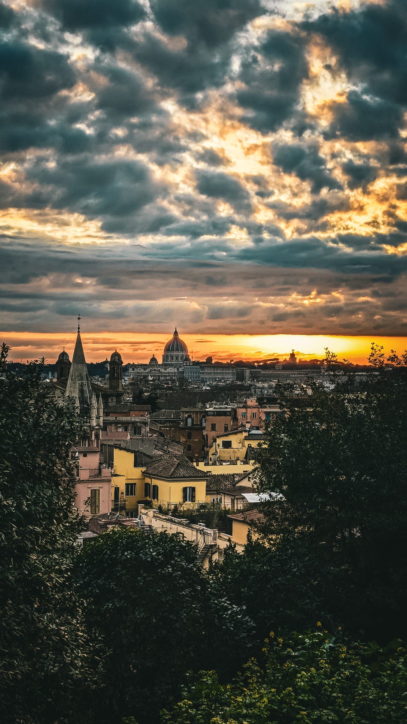 Rooftops of an old city at sunset, a great dome on the skyline under broken clouds