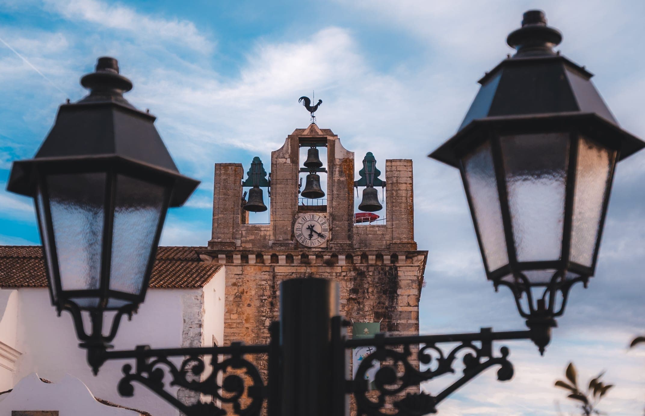 Two black street lanterns framing a white bell gable with three bells