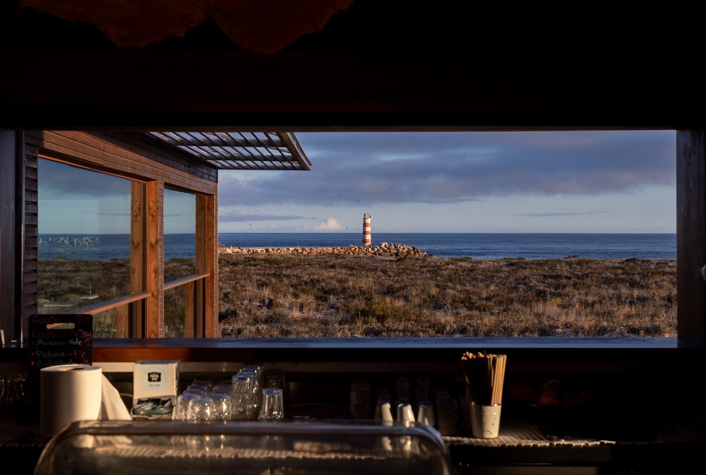 A café window looking out on a coast with a red and white lighthouse