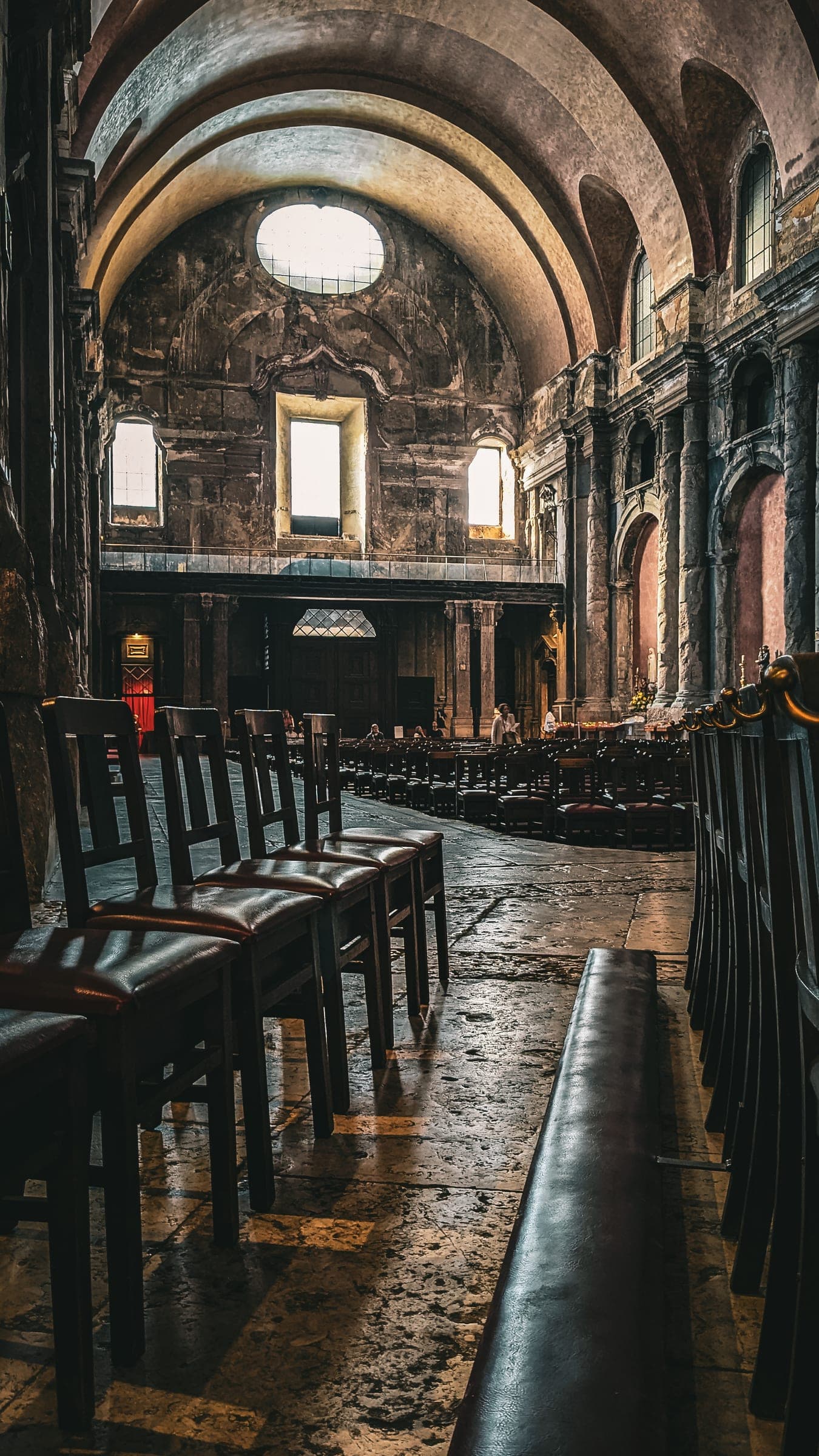 The dim interior of an old church, rows of wooden chairs under a high vault
