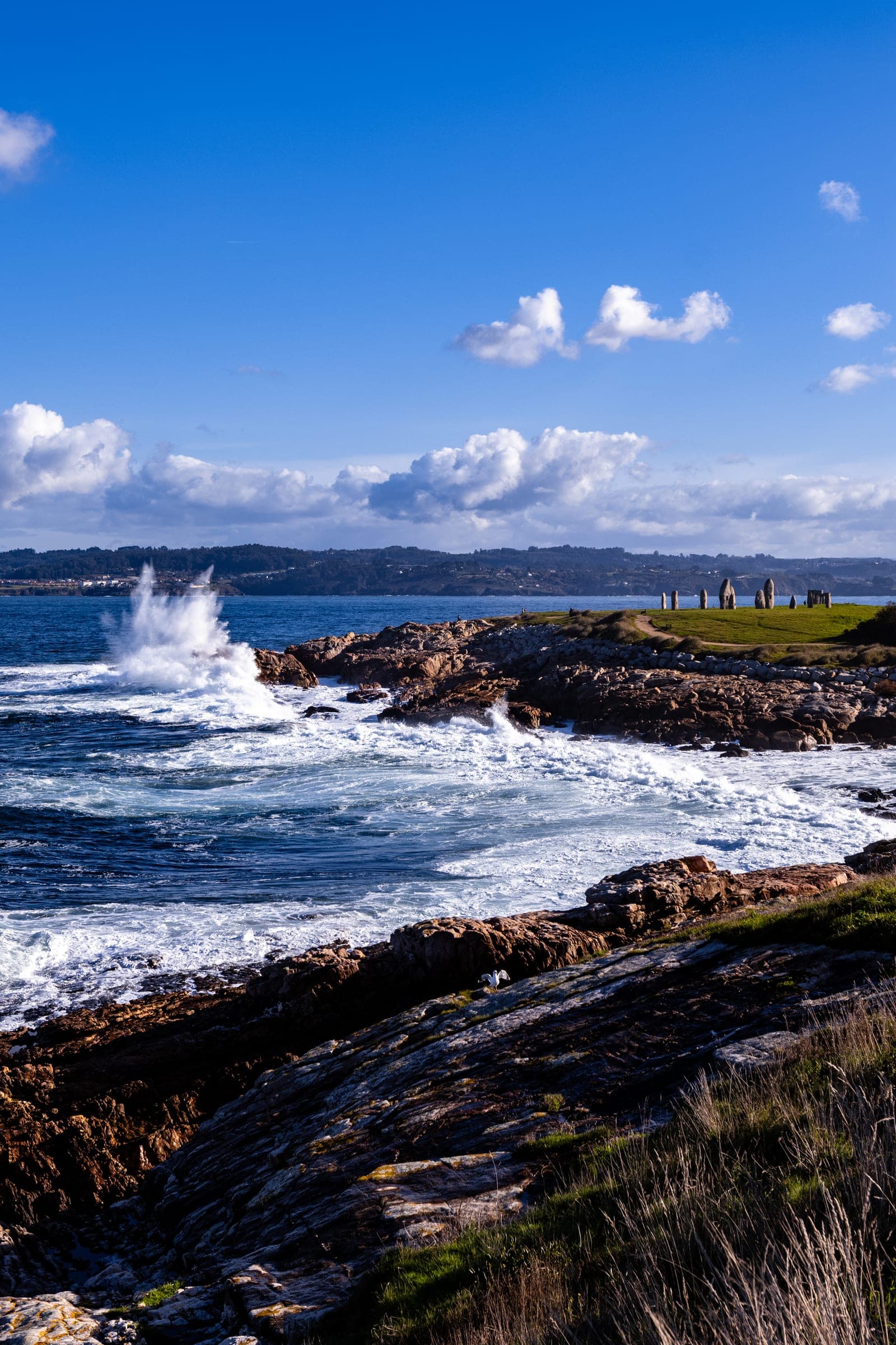 Waves breaking on dark rocks under a blue sky with small clouds