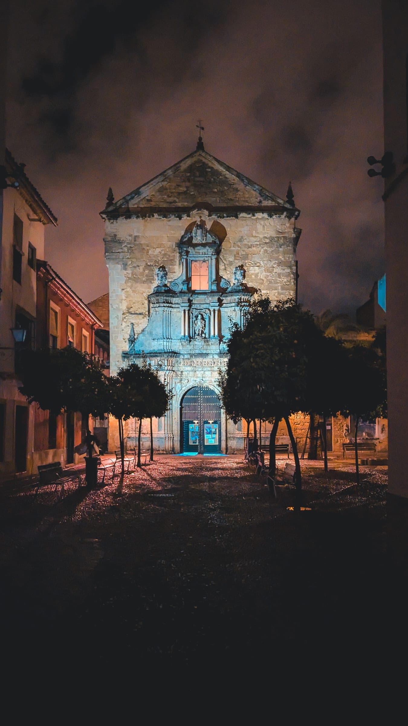 A lit church façade at night at the end of a street lined with trees