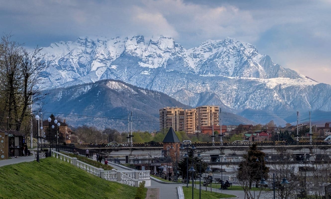 Snow-covered mountains above Vladikavkaz, a green park in the foreground