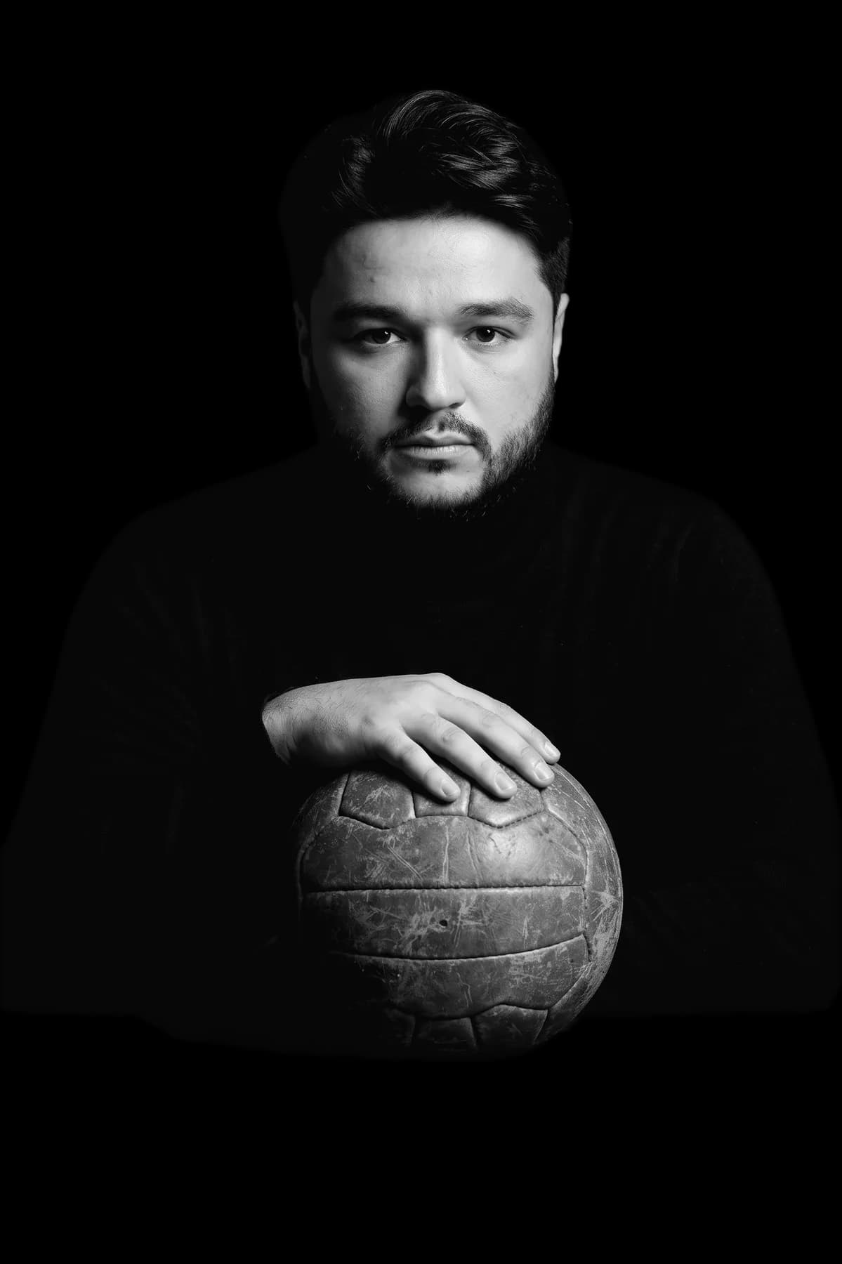 Arsen Dzantiev in a black turtleneck, hands resting on an old leather football
