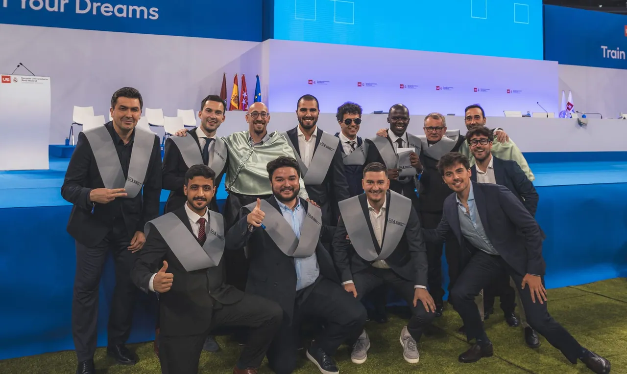 Graduados de la Escuela Universitaria Real Madrid con trajes oscuros y estolas grises en la ceremonia del Bernabéu