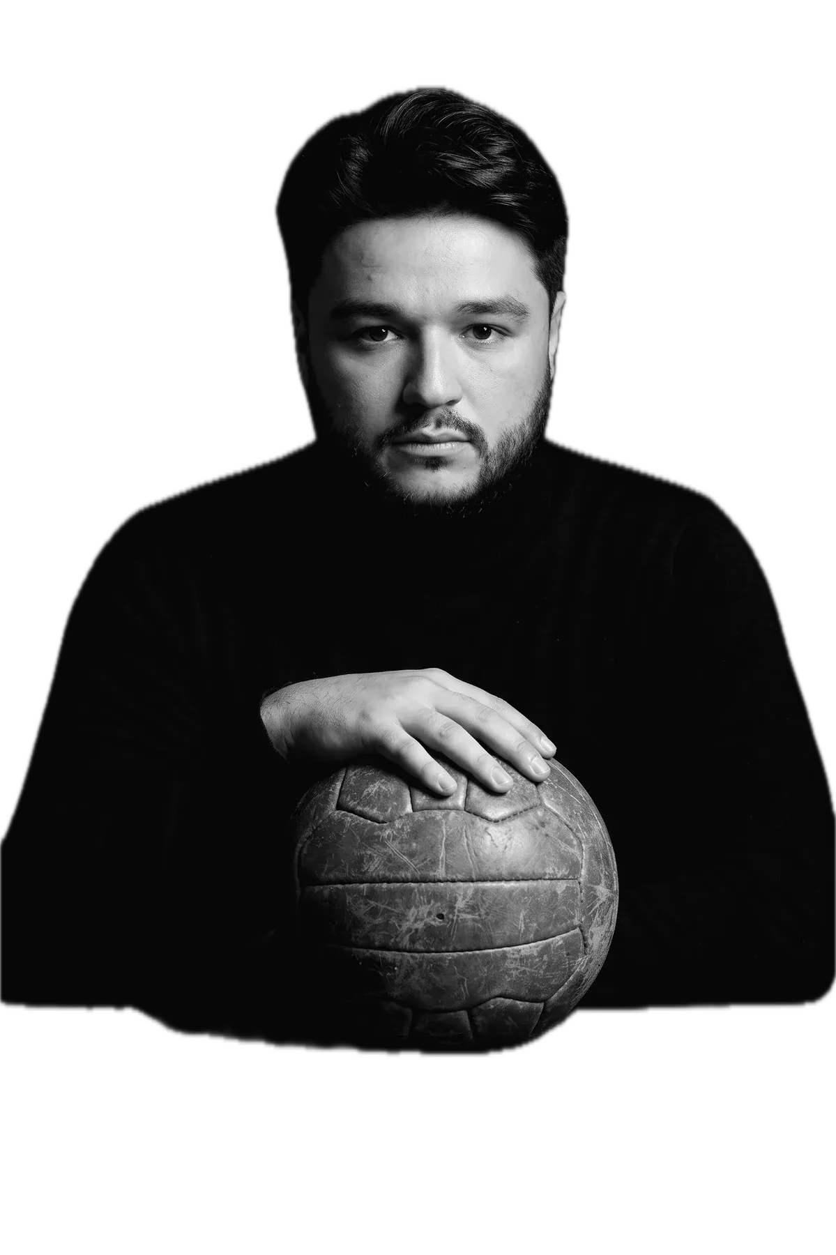 Arsen Dzantiev con jersey negro de cuello alto, las manos sobre un antiguo balón de fútbol de cuero